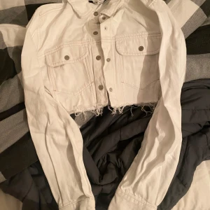 Vit croppad jeansjacka från Zara - Säljer en snygg vit croppad jeansjacka från Zara. Jackan har knappar framtill och två bröstfickor med knappstängning. Perfekt för en trendig look!