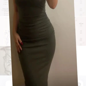 Grön långklänning med drapering - Snygg grön långklänning med draperad detalj på sidan. Klänningen är ärmlös och har en elegant och stilren design. Perfekt för en chic look.