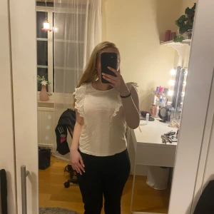 Vit topp med volangdetaljer - Säljer en söt vit topp med volangdetaljer på axlarna.  Från lindex. Använd fåtal gånger. Kommer ej till användning 