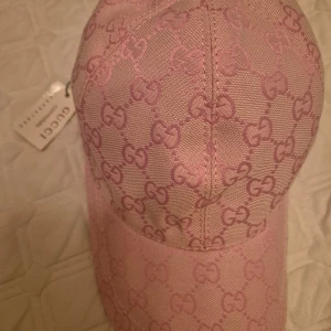 Rosa keps från Gucci - Snygg rosa keps från Gucci med deras ikoniska mönster. Kepsen har en justerbar rem baktill för perfekt passform. Perfekt för att ge din outfit en lyxig touch.