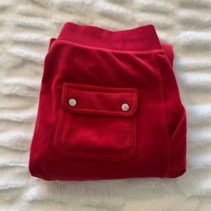 Röda mjukisbyxor från Juicy Couture - Snygga röda mjukisbyxor från Juicy Couture med praktiska fickor och knappar. Byxorna har en bekväm passform och är perfekta för en avslappnad stil. De är tillverkade i ett mjukt material som känns skönt mot huden. Priset går att pruta.
