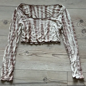 Beige och brun långärmad croppad topp - Säljer en unik beige och brun långärmad topp med ett vågigt mönster. Toppen är croppad och har en rundad halslinje. Perfekt för en trendig look!