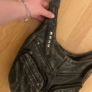 2000s väska med nitar - Snygg svart axelväska i skinn med flera dragkedjor och coola nitar på axelremmen. Perfekt för att ge din outfit en edgy touch. Väskan har flera fack för enkel organisering!! Köpt för 700 💕