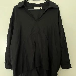 InWear svart blus i linne, storlek 42 - Svart blus i linne med krage och v-ringning från Inwear i storlek 42. Långa ärmar med manschetter. Asymmetrisk fåll, längre baktill. I nyskick. 52% linne och 48% viskos.   Mått:  Längd ca 58 (fram) och 70 cm (bak) Byst ca 50 cm