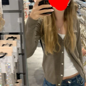 Beige kofta från Zara - Säljer en stilren beige kofta från Zara med v-ringning och knappar framtill. Perfekt för lager-på-lager och passar till många olika outfits. Koftan har långa ärmar och är tillverkad i ett mjukt material.