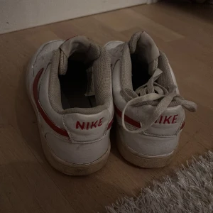 Vita och röda Nike sneakers - Säljer ett par klassiska vita Nike sneakers med röda detaljer. Skorna har snörning och en rund tå. Perfekta för en avslappnad stil. Snörna kommer vid sidan. Även nymålade i orginal färgerna så ser extra nya ut. 
