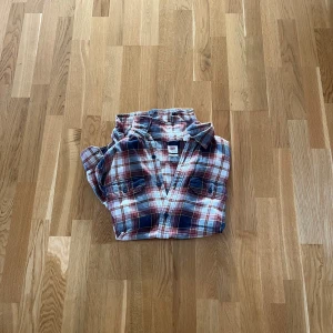 Rutig flanellskjorta från Levis - Säljer en klassisk rutig flanellskjorta i rött, blått och vitt. Skjortan har långa ärmar och knappar framtill samt två bröstfickor med knappar. Perfekt för en avslappnad stil.