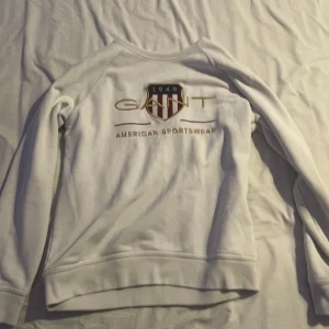 Vit sweatshirt från GANT - Säljer en stilren vit sweatshirt från GANT med tryck på bröstet. Tröjan har långaärmar. Perfekt för en avslappnad stil.