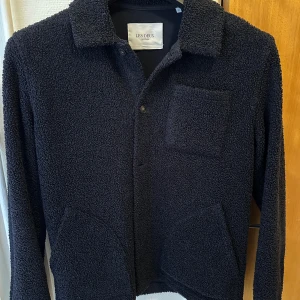 Mörkblå teddyjacka från Les Deux - Säljer en snygg mörkblå teddyjacka från Les Deux. Jackan har en klassisk krage och knäppning framtill. Den är långärmad och har två fickor framtill samt en bröstficka. Perfekt för kyligare dagar! Pris kan diskuteras.