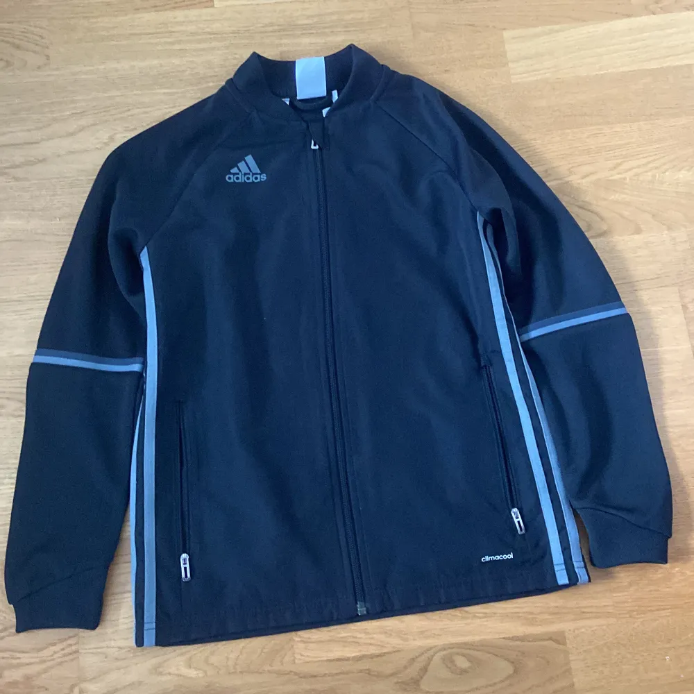 Säljer en svart träningsjacka från Adidas med Climacool-teknologi🔥 Jackan har dragkedja framtill och två fickor med dragkedjor. Den har långa ärmar och grå detaljer längs sidorna och ärmarna. Perfekt för sport och träning ⚽️ . Takit.
