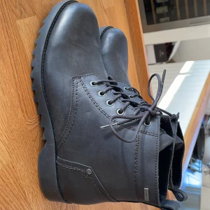 Svarta skinnkängor med Gore-Tex - Säljer ett par svarta skinnkängor med snörning och Gore-Tex-material. Perfekta för alla väder med en robust sula och stilren design. Kängorna har en diskret logga och är tillverkade i Portugal,  i mjukt skinn. Nypris 1900:-
