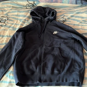 Blå hoodie från Nike i M - Säljer en svart hoodie från Nike med dragkedja och huva. Den har en broderad Nike-logga på bröstet och praktiska fickor framtill. Perfekt för en avslappnad stil. Lyssna, jag vet att den är skrynklig men det går ju fint att stryka den om ni önskar ❤️❤️❤️