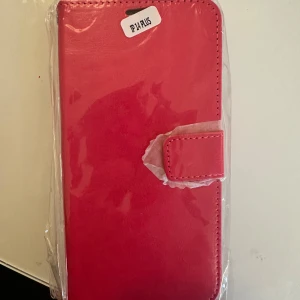 Rosa plånboksväska för iPhone 14 Plus - Snygg och praktisk rosa plånboksväska för iPhone 14 Plus. Väskan har en magnetisk stängning och är tillverkad i syntetmaterial. Perfekt för att skydda din telefon med stil.