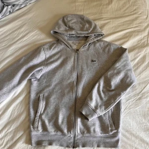 Grå hoodie från Lacoste - Säljer en skön, snygg Lacoste hoodie med dragkedja. Köpte nyligen för 500 beggat men säljer för lite billigare för lite användning. 