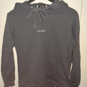 Grå hoodie från Les Deux - Säljer en stilren grå hoodie från Les Deux med justerbar huva och känguruficka. Perfekt för en avslappnad look. Märkesloggan är diskret placerad på bröstet.
