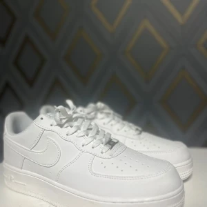 Vita Nike Air Force 1 - Säljer ett par klassiska vita Nike Air Force. Använda en gång för att dom är för stora. Skorna har en stilren design med snörning och den ikoniska Nike-loggan på sidan. Perfekta för en casual look.