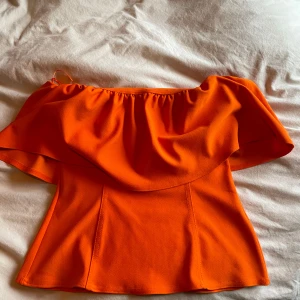 Orange offshoulder topp - Snygg orange offshoulder topp med volangdetaljer. Perfekt för sommarens alla tillfällen. Den har en lös passform och tunna axelband för en luftig känsla. Från Zara i storlek L