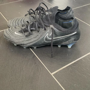 Nike Phantom GX elite svarta  - Snygga svarta fotbollsskor från Nike med snörning och en stilren design. Skorna har en strumpliknande passform och är perfekta för spel på alla planer, men speciellt konstgräs. Använda i någon månad men i bra skick. Skick 8/10. 
