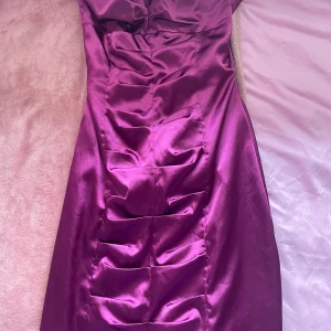 Mörklila klänning från Gina Tricot - Snygg mörklila klänning från Gina Tricot i satin. Klänningen har en elegant passform med veckade detaljer framtill. Perfekt för en festlig kväll!