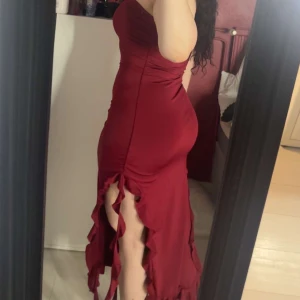 Vinröd klänning från Shein - Säljer en elegant vinröd klänning från Shein. Klänningen är axelbandslös och har en tight passform med volangdetaljer och slitsar längs nederkanten. Perfekt för en festlig kväll! Har aldrig tagit på mig den, utan hann bara ej lämna tillbaka den och därmed säljer jag den!  Jag har storlek 40/M men denna passar även en 38 och en 42! 