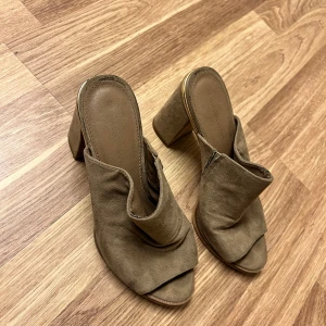 Bruna mocka sandaler med klack - Snygga bruna sandaler i mocka med öppen tå och klack. Perfekta för en stilren look med en bekväm passform. De har en modern design som passar till många olika outfits.