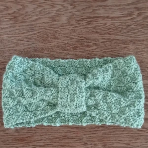 Grönt virkad pannband  - Snyggt grönt virkad pannband med ett fint mönster och en dekorativ knut framtill. Perfekt för att värma öronen och  ge en stilfull touch till din outfit. Hemvrirkad