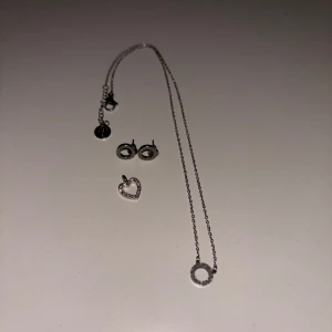 Smyckeset i silver med halsband och örhängen - Elegant smyckeset från Edblad i silver som inkluderar ett halsband med en cirkelberlock och ett par matchande örhängen. Det tillkommer en hjärtformad berlock på köpet men man kan också välja att köpa det var för sig.