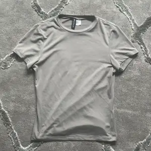 Säljer en stilren grå t-shirt från H&M. Den har en normal passform och är tillverkad i ett mjukt syntetmaterial. Perfekt för en avslappnad look.