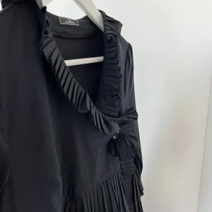 Svart blus från By Malene Birger - Elegant svart blus från By Malene Birger med volangdetaljer och väldigt snygga detaljer överlag. Modellen passar många och går att klä upp och ner enkelt