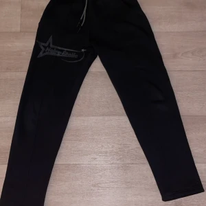 Svarta mjukisbyxor med tryck - Svarta mjukisbyxor med dragsko i midjan och en stor stjärnformad tryckdetalj på ena benet. Byxorna har en bakficka och är perfekta för en avslappnad stil. Finns i storlekar S, M och L.
