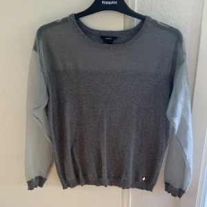 Grå tröja med meshärmar från Lindex - Säljer en grå tröja från Lindex med transparenta meshärmar. Tröjan har rund halsringning och ribbade muddar vid ärmslut och nederkant. Perfekt för dig som vill ha en stilren men ändå unik look.