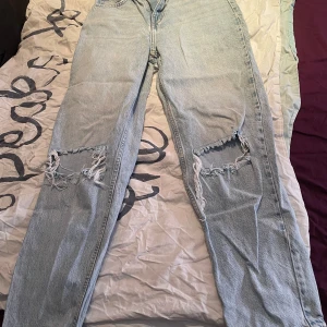 Ljusblå ripped jeans från Gina tricot - Säljer ett par ljusblå jeans från Gina tricot i storlek 34. Byxorna har raka ben och stora slitningar vid knäna. Dom är använda några gånger men har inte använts på ett väldigt långt tag.