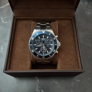 Silverfärgad kronografklocka från Champion - Stilren herrklocka från Champion med blå urtavla och silverfärgad länk i rostfritt stål. Klockan har kronograffunktion och tydliga indexmarkeringar. Perfekt accessoar för dig som gillar klassisk design.