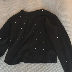 Svart tröja med paljettdetaljer från H&M - Säljer en svart tröja från H&M i storlek XS. Tröjan har långa ärmar och är dekorerad med små paljetter över hela framsidan. Rund halsringning och ribbade muddar vid ärmslut och nederkant.