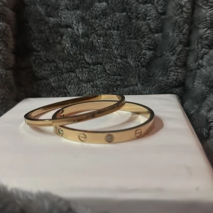 Bronsfärgad armband med stenar - Två stilrena armband i bronsfärgad, varav ett är dekorerat med små klara stenar och ingraverade cirkelmotiv. Båda armbanden har en elegant och minimalistisk design som passar perfekt till accessoar-samlingen. Rostfritt!!