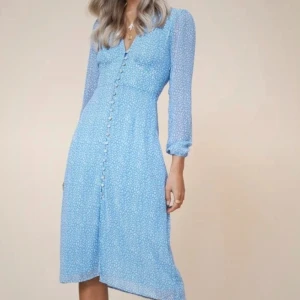 Adoore strl XS - Fint skick! Supersöt ljusblå klänning från Adoore med små vita blommor, v-ringning och knappar framtill. Klänningen har trekvartsärm och en lätt utställd kjol som slutar strax under knät. Perfekt för vår och sommar! 