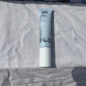 Sensitive Skin Eye Cream från Urtekram - En ljusblå tub med vit kork, innehållande ögonkräm för känslig hud. Produkten är vegansk och innehåller hyaluronsyra och avokadoolja. Tuben rymmer 15 ml och är smidig att ta med i necessären.