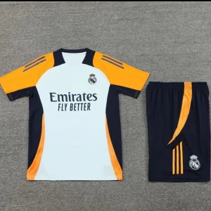 Real Madrid fotbollströja med shorts - Säljer en Real Madrid fotbollströja med tillhörande shorts. Tröjan är vit med svarta och orange detaljer, kortärmad och har klubbmärke samt Adidas-logga. Materialet är lätt och andas, perfekt för träning eller match.