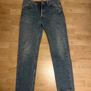Levis 505 blå jeansbyxor - Klassiska blå Levis 501 jeans med raka ben och femficksdesign. Byxorna har normal passform, knappgylf och tydliga Levis-detaljer som röd etikett och läderpatch bak i midjan. Perfekta för en tidlös stil.