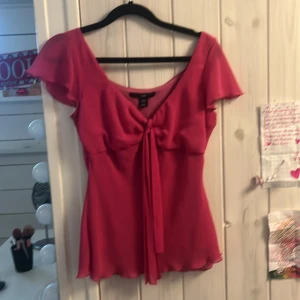 Rosa blus med knyt från H&M - Säljer en söt rosa blus från H&M med korta volangärmar och knyt framtill. Blusen har v-ringning och är tillverkad i ett lätt, luftigt material som ger ett fint fall.