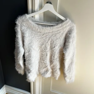 Vit fluffig tröja från Gina Tricot - Supermjuk och fluffig vit tröja från Gina Tricot. Tröjan har lång ärm och en lös, lite off shoulder passform. Perfekt för alla outfits när du vill vara både bekväm och snygg.