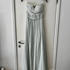 Ljusgrön axelbandslös långklänning - Elegant ljusgrön långklänning med axelbandslös design och vacker drapering framtill. Lite sliten längst ner men märks inte av när den är på!