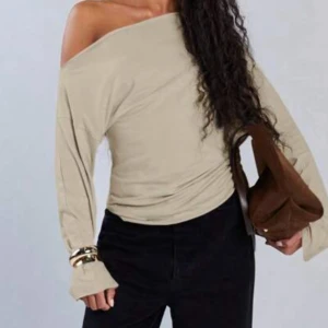 Beige offshoulder långärmad topp - Trendig beige topp med offshoulder-design och långa ärmar. Perfekt för dig som vill ha en stilren och modern look. Mjuk och skön att bära, passar till många olika outfits.