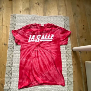 Röd tie-dye t-shirt från Gildan med LA SALLE-tryck - Säljer en röd och vit tie-dye t-shirt från Gildan med LA SALLE-tryck på bröstet. T-shirten har klassisk passform och är tillverkad i bomull. Perfekt för dig som vill sticka ut med en färgstark och unik stil. Jag har använd den 1 eller 2 gånger så den är ganska nytt skick