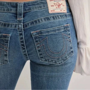 Blå bootcut jeans från True Religion - Säljer ett par klassiska blå bootcut jeans från True Religion med ikoniska bakfickor och ljus kontrastsöm. Jeansen är aldrig använda, bara provade!