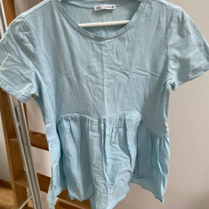Ljusblå topp från Zara - Söt ljusblå topp från Zara med korta ärmar och rund halsringning. Klänningen har en lös passform och rynkad midja. 