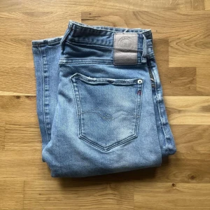 Replay jeans  - Säljer ett par ljusblå jeansbyxor från Replay med klassisk femficksdesign och raka ben. Jeansen har en snygg tvättad look och detaljer som Replay-logga på bakfickan och patch vid linningen. Perfekta för en avslappnad stil. Längd 98cm