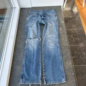 Blå bootcut jeans från Wrangler - Säljer ett par blå bootcut jeans från Wrangler med slitningar och hål på ena knät. Midjemått: ca 40 cm midjehöjd: 24 cm innerbenslängd: ca 80 cm💕Lite slitna längst ner vilket inte är något man tänker på när man har på sig jeansen, men det syns på sista bilderna💕