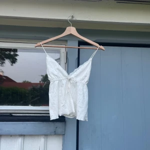 Vitt linne  - Säljer en vit linnetopp med tunna axelband och v-ringning. Toppen har fina spetsdetaljer, korsad rygg och knyt framtill. Perfekt för varma dagar och ger en romantisk känsla.