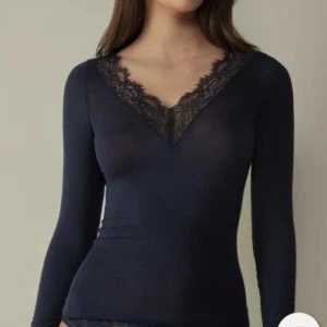 Mörkblå intimissimi tröja med spets - Snygg mörkblå topp med lång ärm och djup v-ringning dekorerad med spets. Toppens material är tunt och följsamt, perfekt för lager-på-lager eller som en elegant detalj i vardagslooken. Den har några lösa trådar på magen och ett litet hål men man tänker inte på dom enligt mig!!🩷köpt för 500